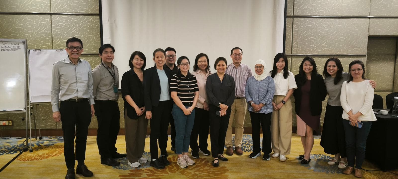 Group photo of participants and facilitators standing together after a workshop in a hotel meeting room