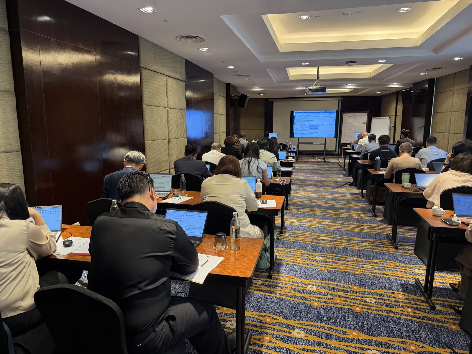 Rows of participants with laptops facing the screen in a hotel ballroom workshop