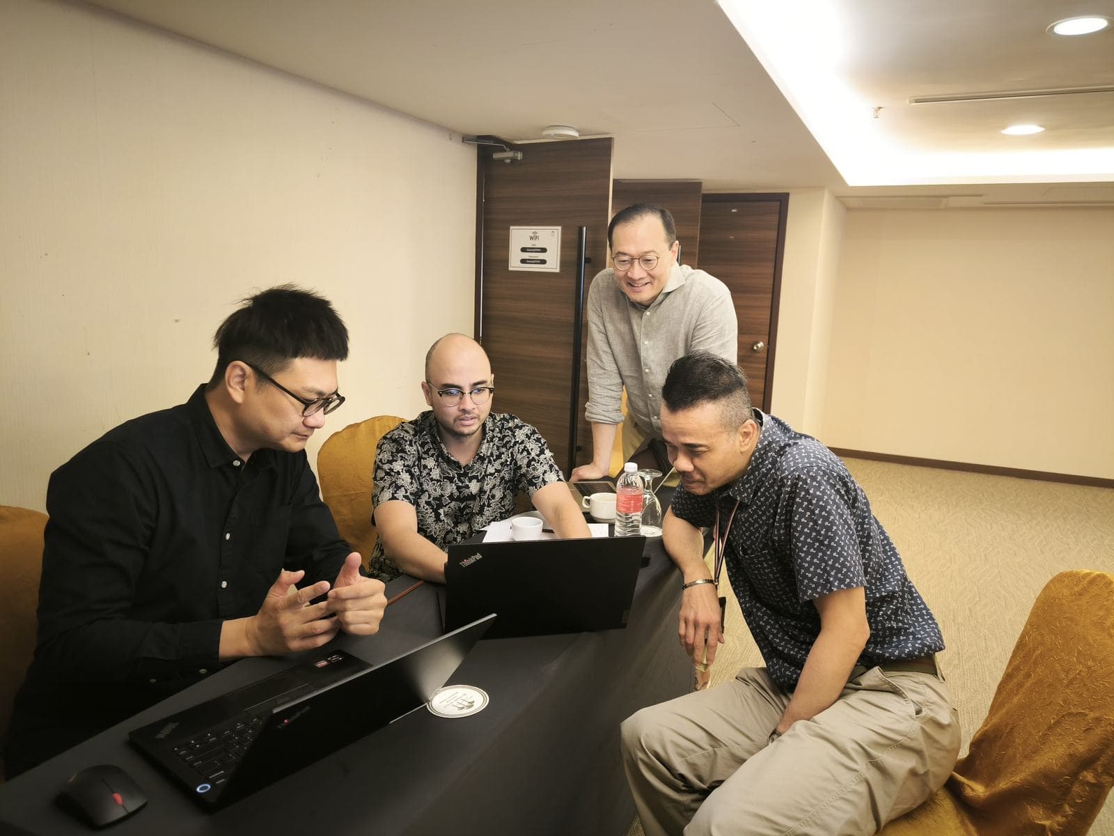Facilitator and participants gathered around a laptop working through an exercise in a hotel function room