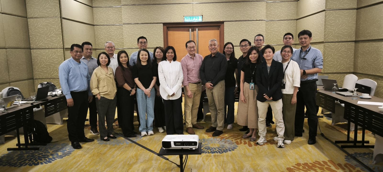 Group photo of workshop participants and facilitators standing together in front of a projector in a hotel function room